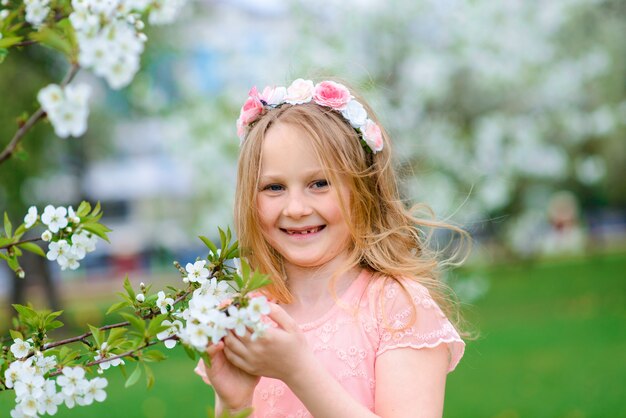 Pretty child girl smiling and playing in flowers of the garden, blooming trees, cherry, apples.