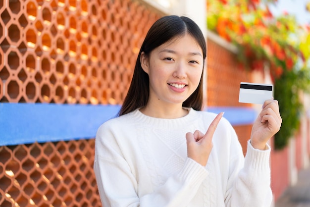 Pretty Chinese woman holding a credit card at outdoors and pointing it