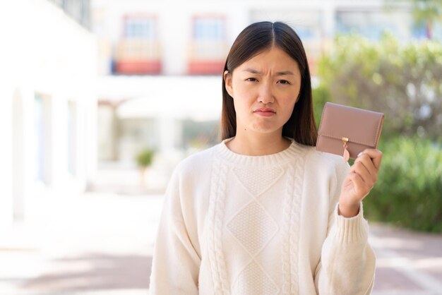 Pretty Chinese woman holding a wallet at outdoors with sad expression