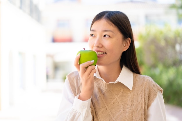 Pretty Chinese woman at outdoors holding an apple with happy expression