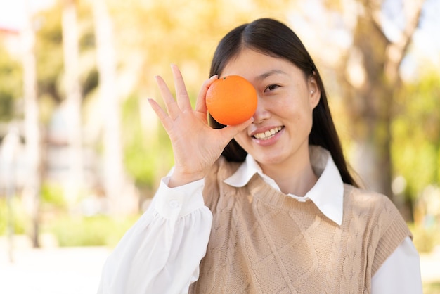 Pretty Chinese woman at outdoors holding an orange with happy expression