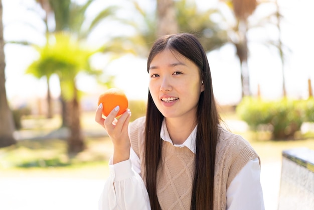 Pretty Chinese woman at outdoors holding an orange