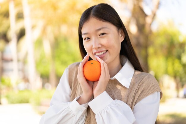 Красивая китаянка на улице держит апельсин