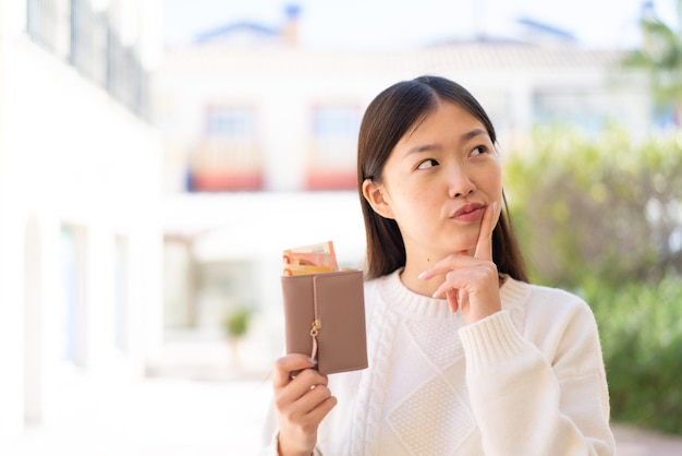 屋外でお金の入った財布を持っているかなり中国人の女性