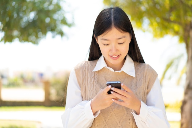 Pretty Chinese woman at outdoors sending a message with the mobile