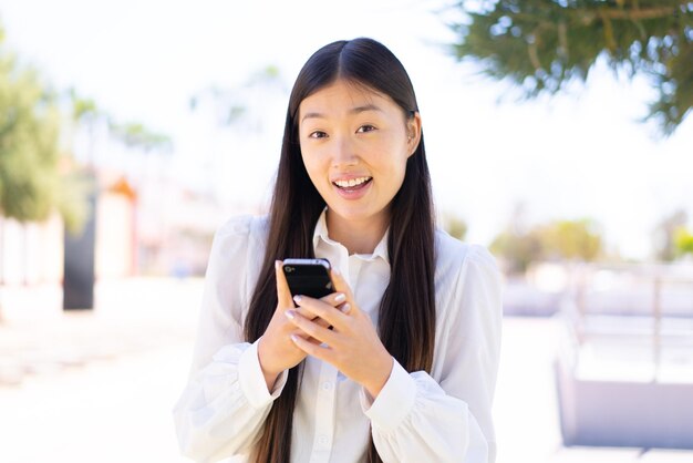 屋外で驚いてメッセージを送信するかなりの中国人女性