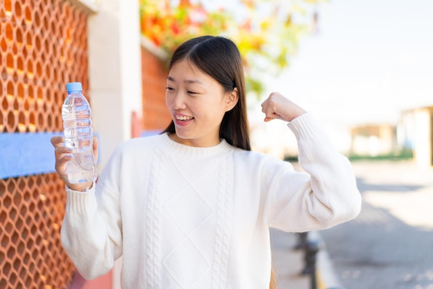 屋外で水の入ったボトルを持って勝利を祝う美しい中国人女性