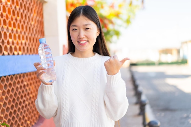 屋外で水の入ったボトルを持ち、側面を指して製品を提示するかなりの中国人女性