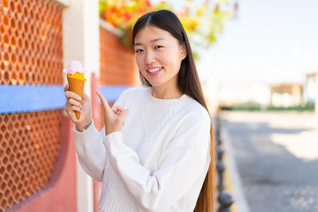 야외에서 코넷 아이스크림을 들고 그것을 가리키는 예쁜 중국 여자