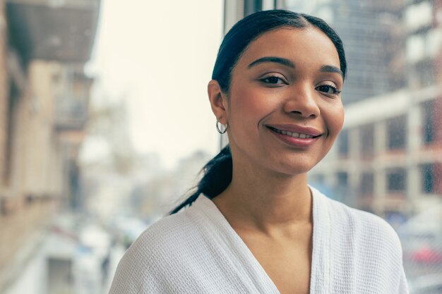 Pretty confident woman smiling to the camera while posing near the window alone