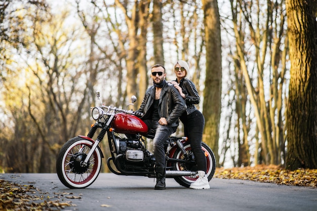 Pretty couple near red motorcycle on the road in the forest  