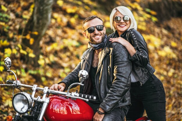 Pretty couple near red motorcycle on the road in the forest