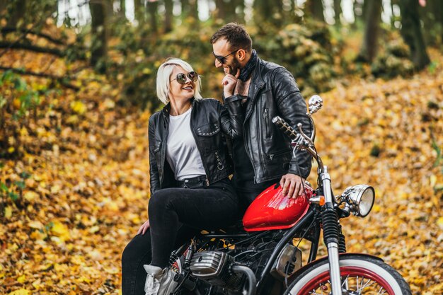 Pretty couple near red motorcycle on the road in the forest