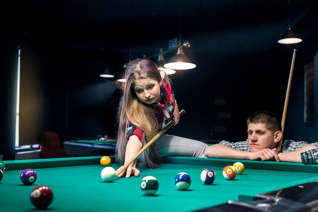 Pretty couple playing billiard, man looking after woman