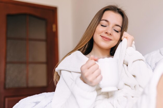 Pretty cute girl drinks coffee from white cup at home