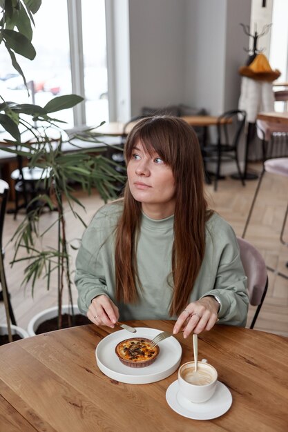 Pretty cute woman sitting in empty cafe eats cake and drinks coffee