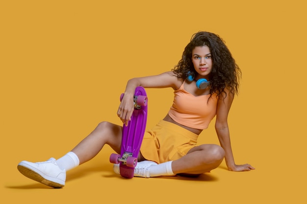 Pretty dark-haired young woman with a skateboard sitting on a floor