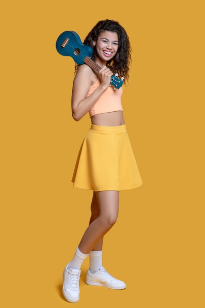 Pretty dark-haired young woman in yellow clothes with ukulele