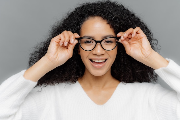 Pretty dark skinned female has minimal makeup, keeps hands on frame of transparent glasses