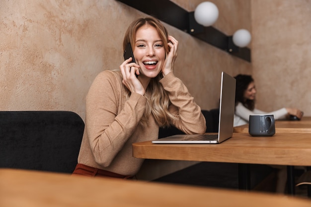 pretty emotional happy girl sitting in cafe talking by mobile phone