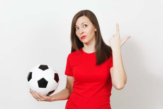 Pretty european young pensive thoughtful woman, football fan or\
player in red uniform holding classic soccer ball isolated on white\
background. sport, play football, health, healthy lifestyle\
concept.