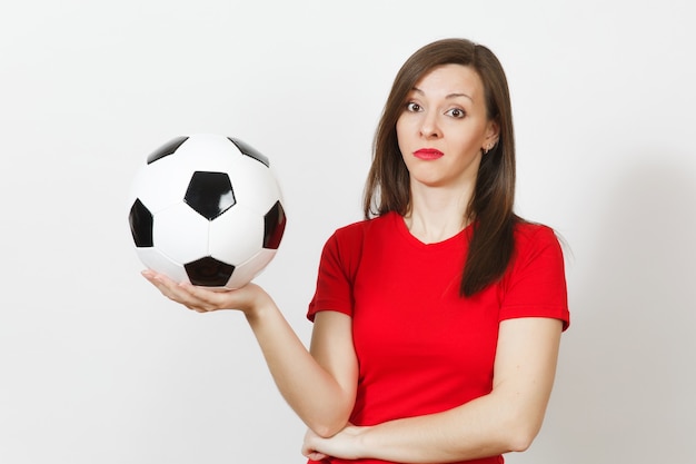 Pretty European young sad upset woman, football fan or player in red uniform holds soccer ball, worries about losing team isolated on white background. Sport, play football, lifestyle concept.