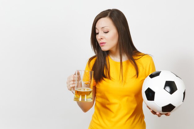 Pretty European young sad upset woman, football fan or player in yellow uniform holds pint mug of beer, worries about losing team isolated on white background. Sport, play football, lifestyle concept.