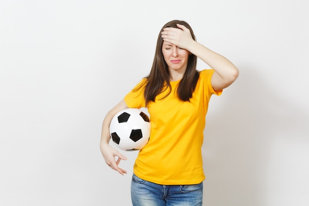 Pretty European young sad upset woman, football fan or player in yellow uniform holds soccer ball, worries about losing team isolated on white background. Sport, play football, lifestyle concept.