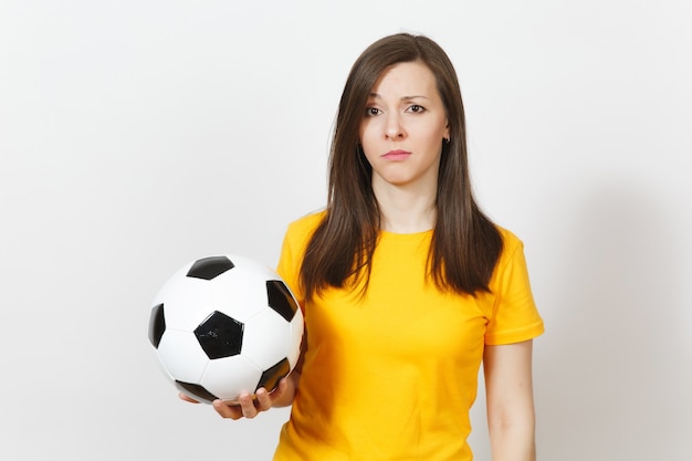 Pretty European young sad upset woman, football fan or player in yellow uniform holds soccer ball, worries about losing team isolated on white background. Sport, play football, lifestyle concept.