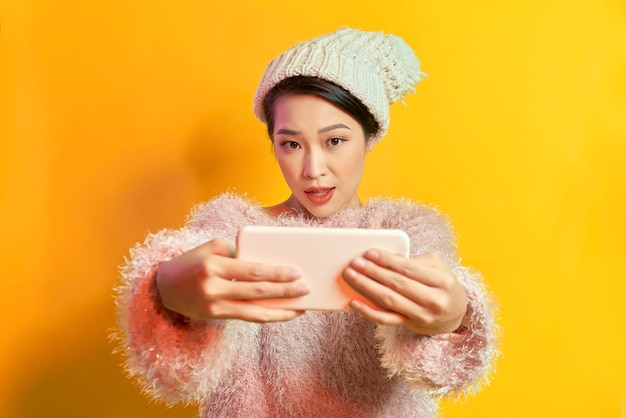 携帯電話で自撮りをしている毛皮のセーターを着たかなり興奮した若い女性