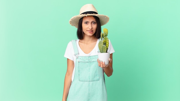 Donna graziosa dell'agricoltore che sembra perplessa e confusa e che tiene un cactus