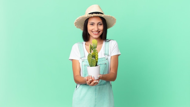 Довольно фермерская женщина счастливо улыбается, дружелюбно предлагает и показывает концепцию и держит кактус