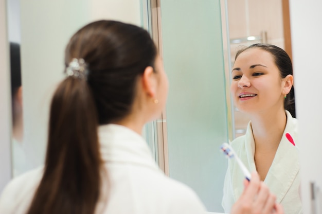 Pretty female brushing her teeth in front of mirror