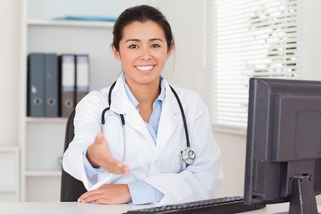 Pretty female doctor inviting somebody to seat while looking at the camera