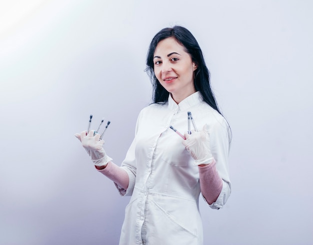 Pretty female doctor wearing white medical robe and holding syringe at gray space