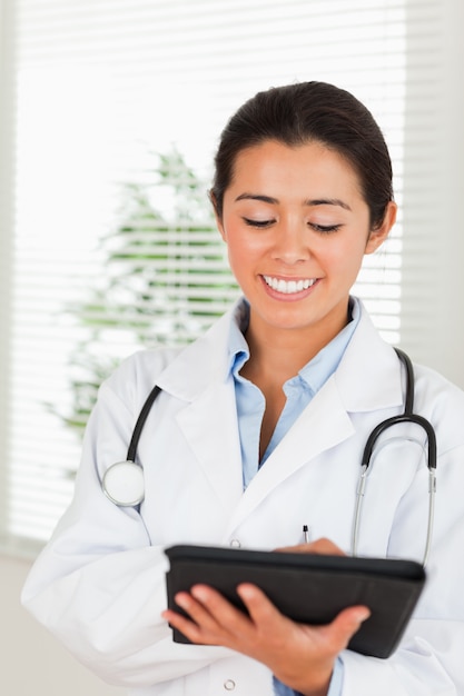 Pretty female doctor with a stethoscope writing on a notebook while standing