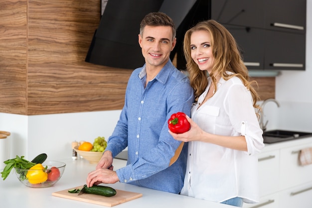 Pretty female and her husband standing and cooking on the kitchen at home