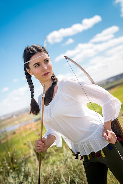 Pretty female hunter with bow plays as native American Indian at outdoor