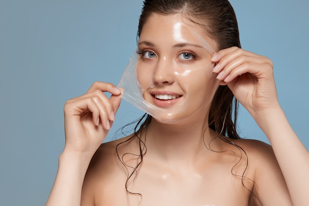 Foto piuttosto femmina rimuovendo la maschera peeling con i capelli bagnati e sorridendo alla telecamera