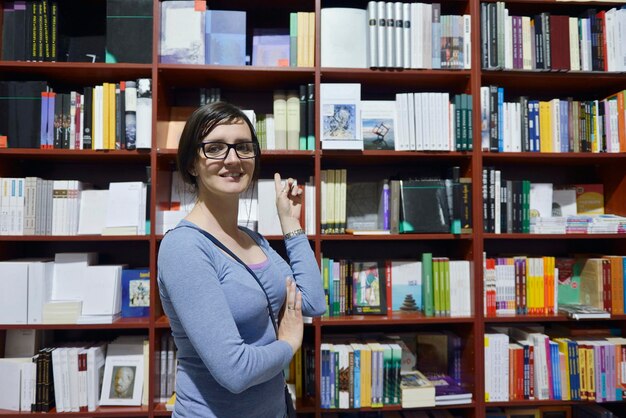 Pretty female student standing at bookshelf in university library store shop  searching for a book