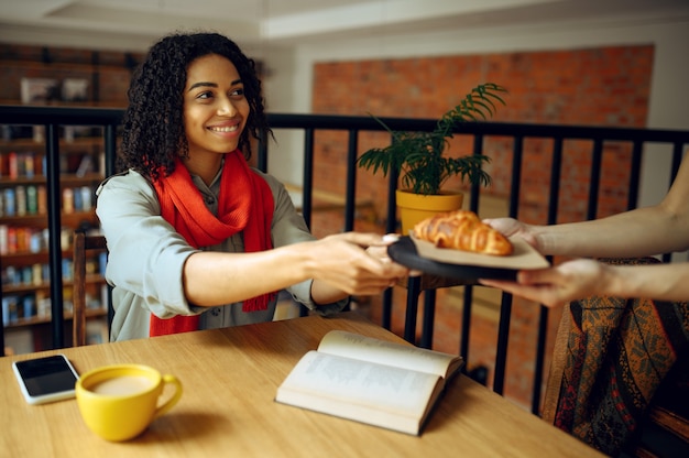 Pretty female student takes croissants in cafe