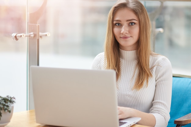 Pretty female student with cute smile prepares for test in cafe.