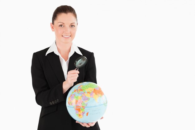 Pretty female in suit holding a globe and using a magnifying glass