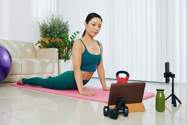 Pretty fit young woman recording video of herself working out at home for her social media