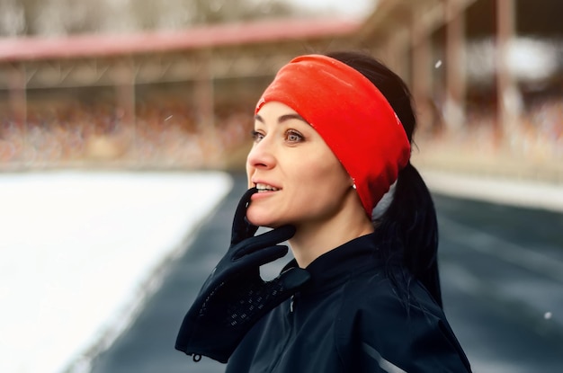 Симпатичная бегунья в красной бандане на зимнем стадионе смотрит в камеру