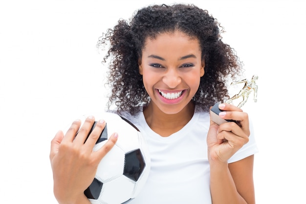 Pretty football player in white holding winners figurine and ball