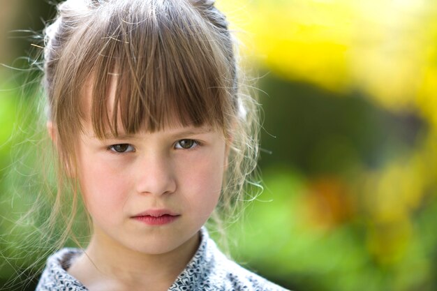 かなり面白い不機嫌そうな若い子の女の子屋外の怒りとぼやけた夏の緑に不満を感じています。子供のかんしゃくのコンセプトです。