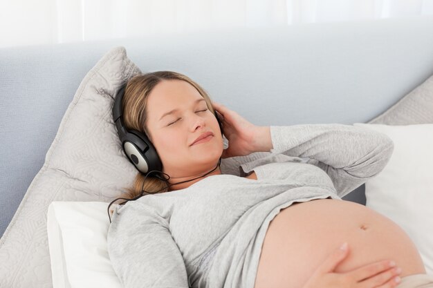 Pretty future mom listening to the music lying on a bed