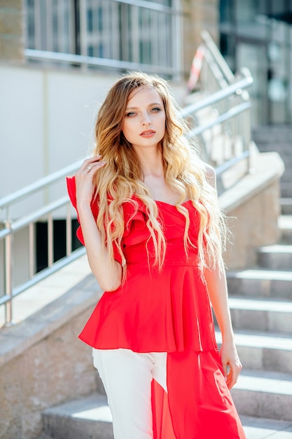 A pretty girl of 20 in an unusual red shirt stands against the backdrop of the city, a large fashion portrait, street fashion