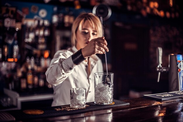 Il barista di bella ragazza dimostra le sue abilità al bancone dietro il bar